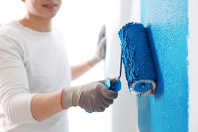 Male decorator painting wall with roller indoors, closeup Photo of Male decorator painting wall with roller indoors, closeup