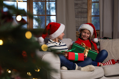 Happy children wearing Santa hats with Christmas gifts on sofa at home Photo of Happy children wearing Santa hats with Christmas gifts on sofa at home