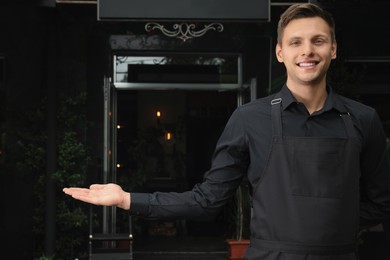 Happy young waiter in uniform near cafe Photo of Happy young waiter in uniform near cafe