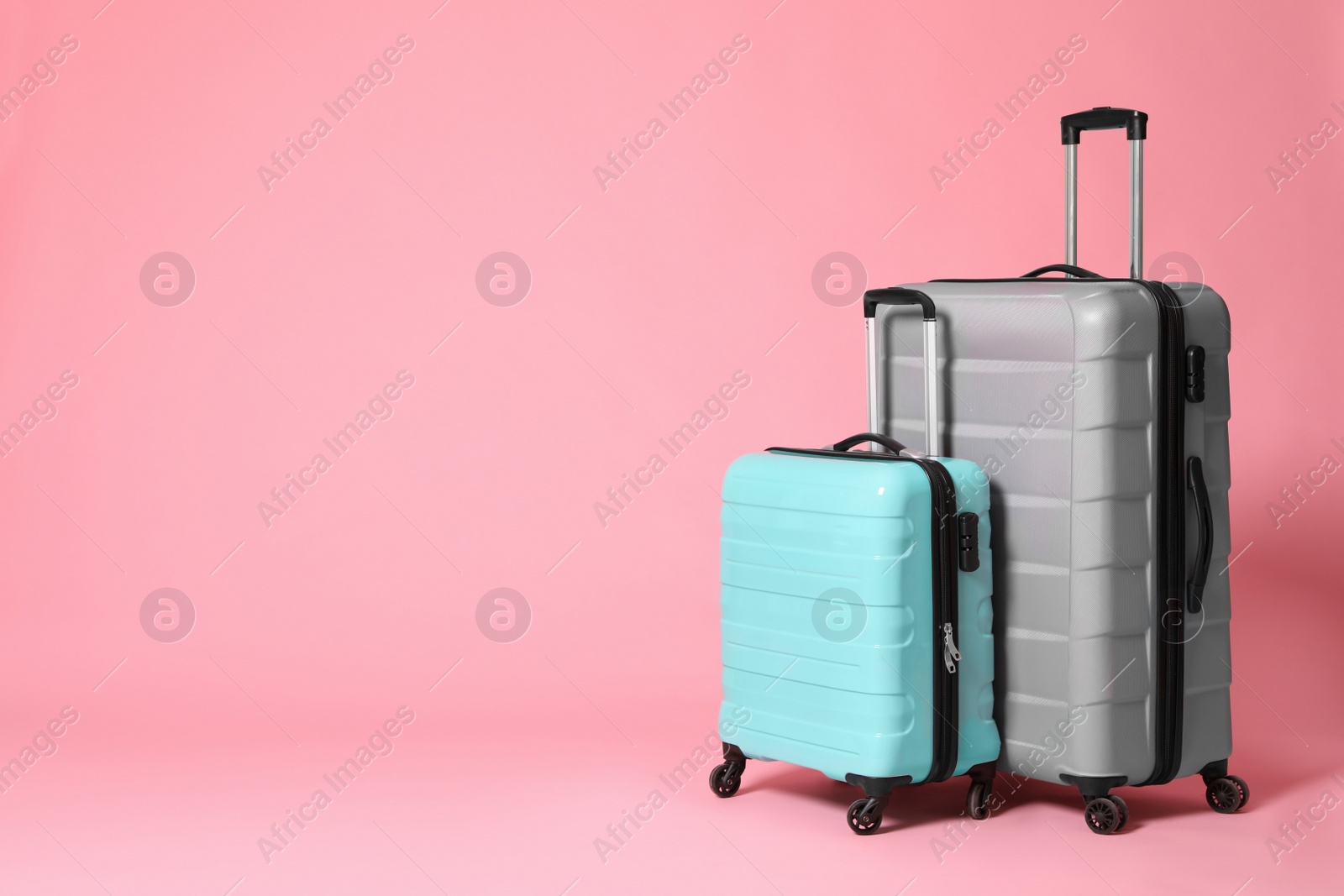 Photo of Stylish grey and turquoise suitcases on pink background. Space for text