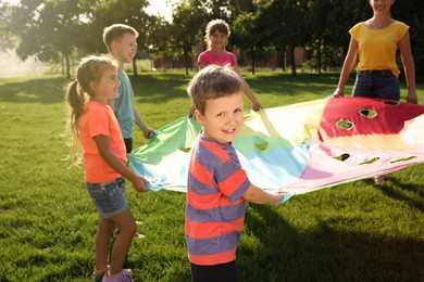 Group of children and teacher playing with rainbow playground parachute on green grass. Summer camp activity Photo of Group of children and teacher playing with rainbow playground parachute on green grass. Summer camp activity