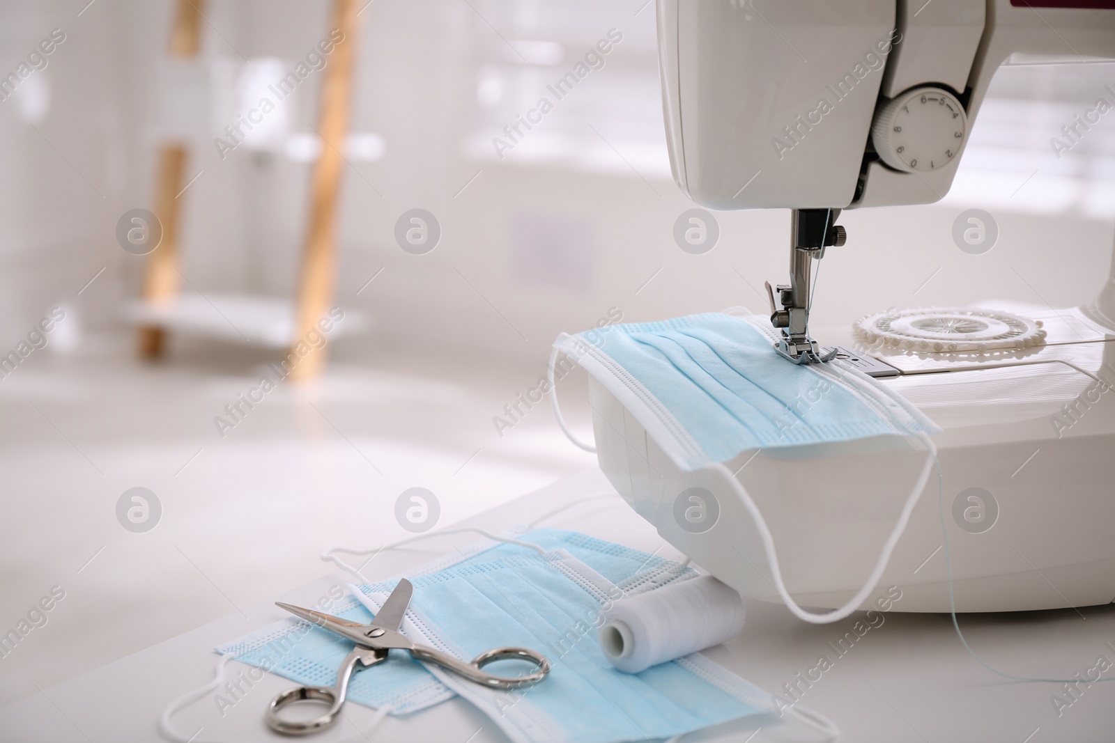 Sewing machine with disposable face mask on table indoors, space for text Photo of Sewing machine with disposable face mask on table indoors, space for text