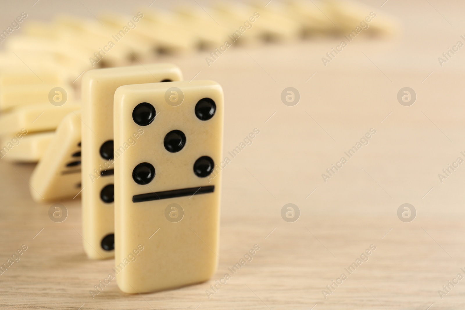 White domino tiles falling on wooden table, closeup. Space for text Photo of White domino tiles falling on wooden table, closeup. Space for text