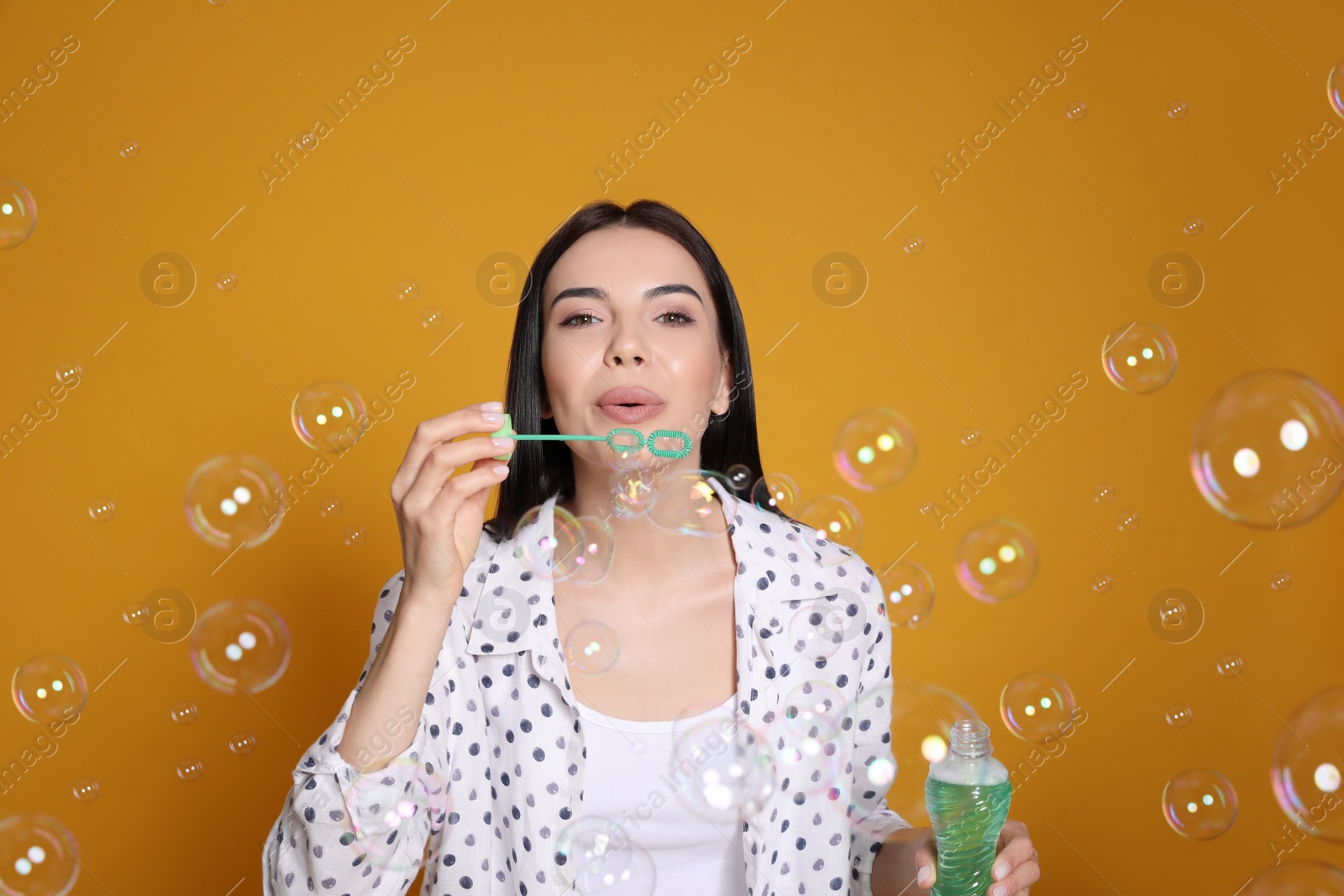 Young woman blowing soap bubbles on yellow background Photo of Young woman blowing soap bubbles on yellow background