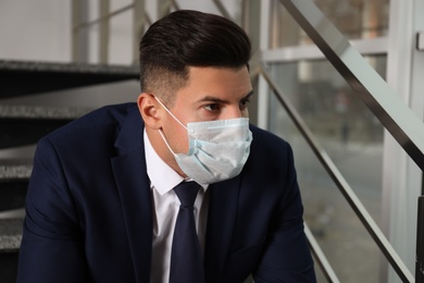 Sad man in protective mask on stairs indoors. Self-isolation during coronavirus pandemic Photo of Sad man in protective mask on stairs indoors. Self-isolation during coronavirus pandemic