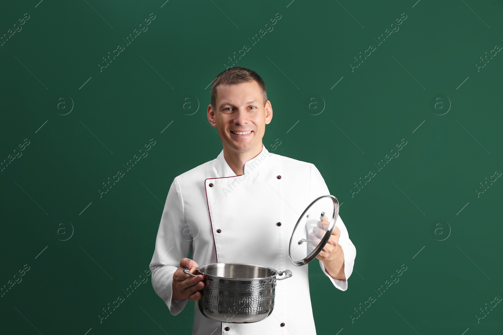 Happy male chef with cooking pot on dark green background Photo of Happy male chef with cooking pot on dark green background