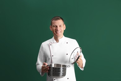 Happy male chef with cooking pot on dark green background Photo of Happy male chef with cooking pot on dark green background