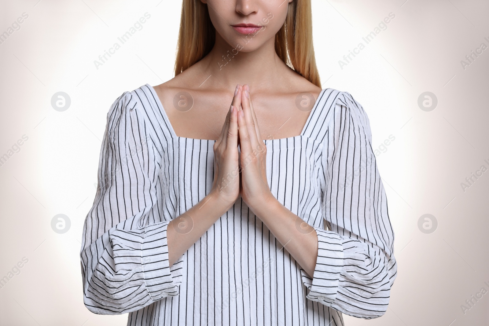 Religious young woman with clasped hands praying against light background, closeup Photo of Religious young woman with clasped hands praying against light background, closeup