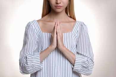 Religious young woman with clasped hands praying against light background, closeup Photo of Religious young woman with clasped hands praying against light background, closeup