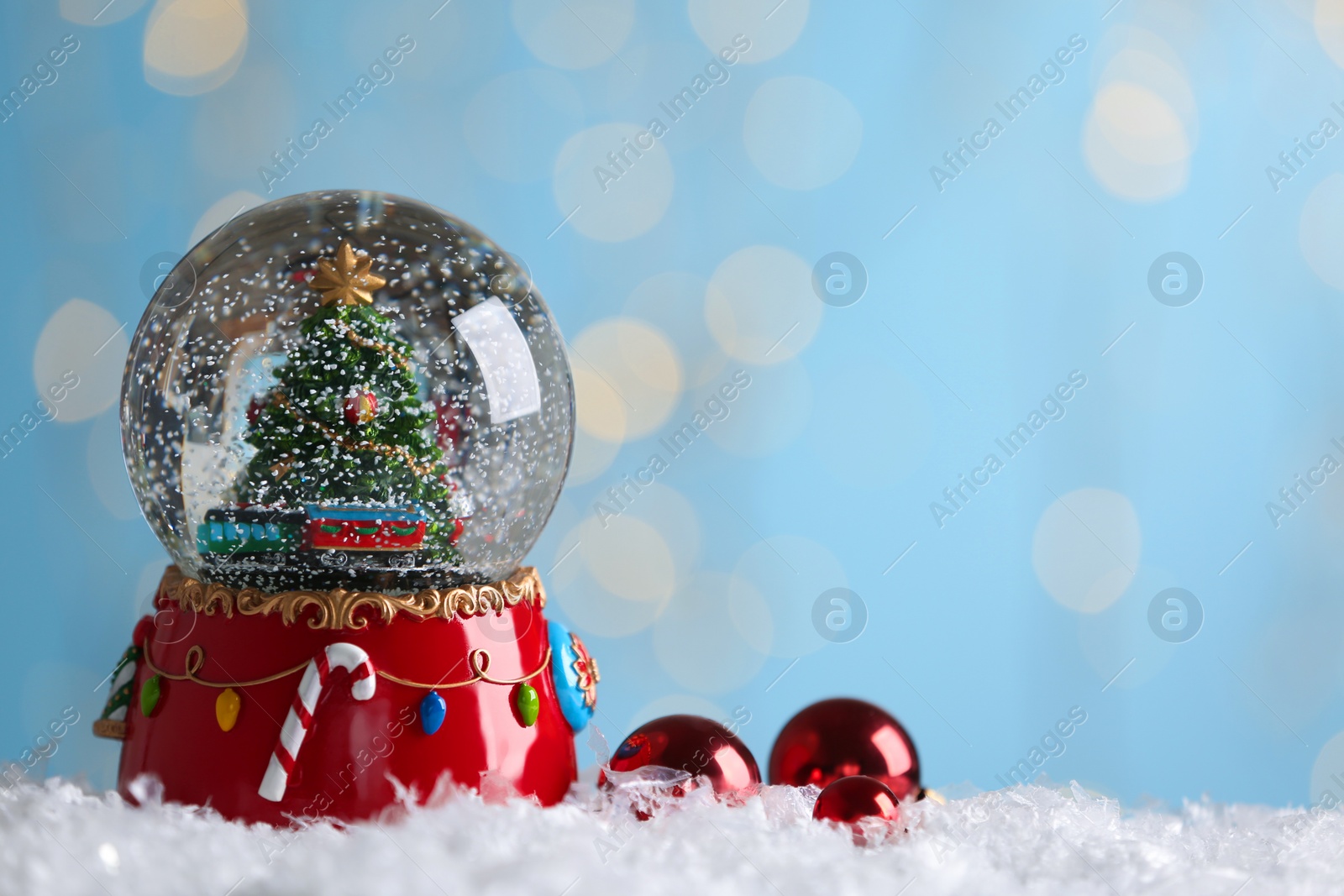 Beautiful snow globe and baubles against blurred Christmas lights. Space for text Photo of Beautiful snow globe and baubles against blurred Christmas lights. Space for text