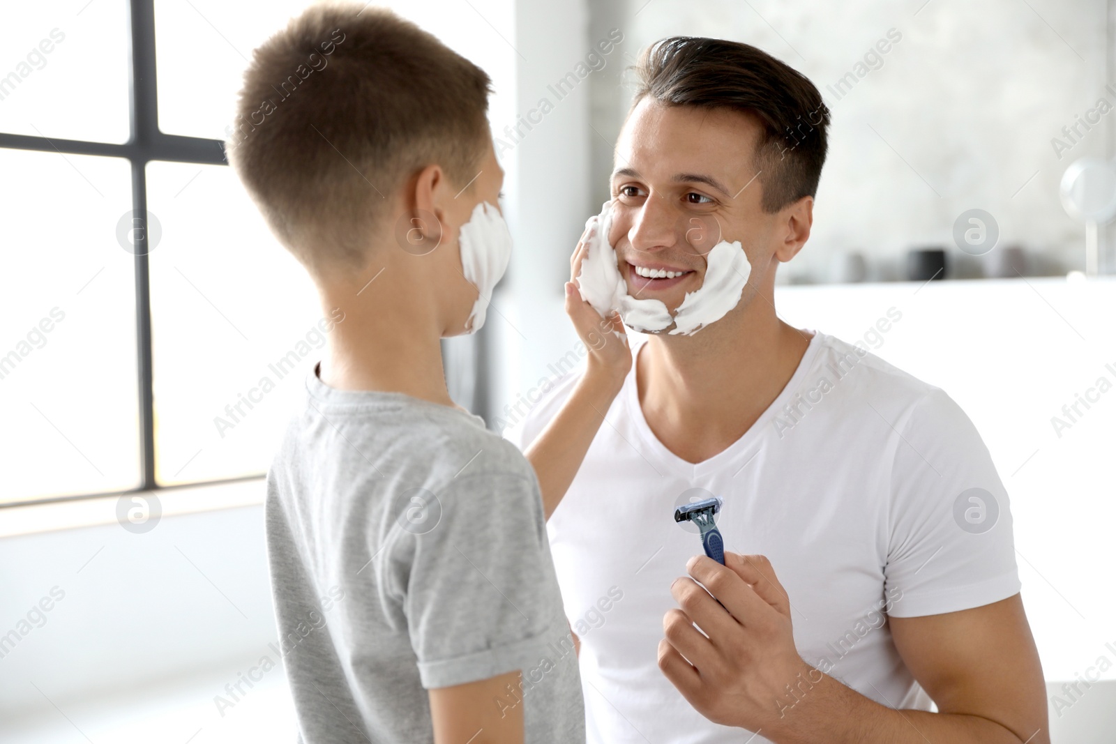 Son applying shaving foam onto father's face in bathroom Photo of Son applying shaving foam onto father's face in bathroom