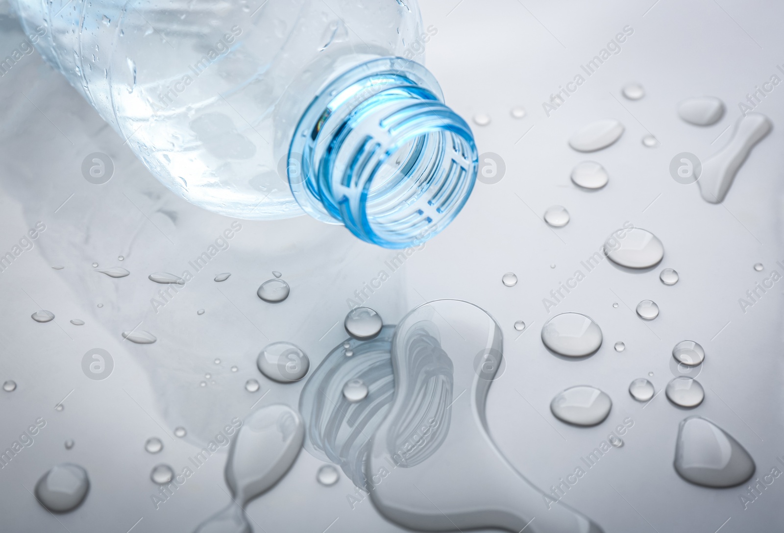 Drops of spilled water and plastic bottle on grey background, closeup Photo of Drops of spilled water and plastic bottle on grey background, closeup