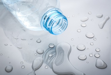 Drops of spilled water and plastic bottle on grey background, closeup Photo of Drops of spilled water and plastic bottle on grey background, closeup