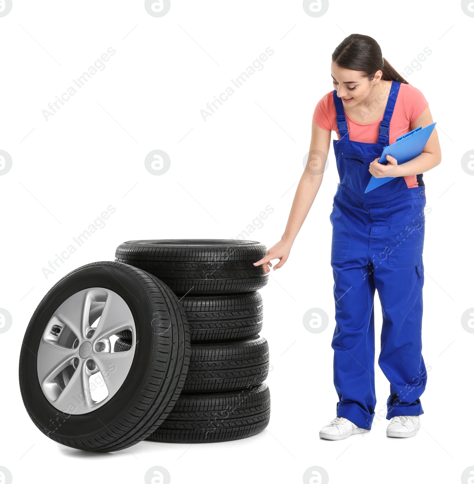 Female mechanic in uniform with car tires and clipboard on white background Photo of Female mechanic in uniform with car tires and clipboard on white background