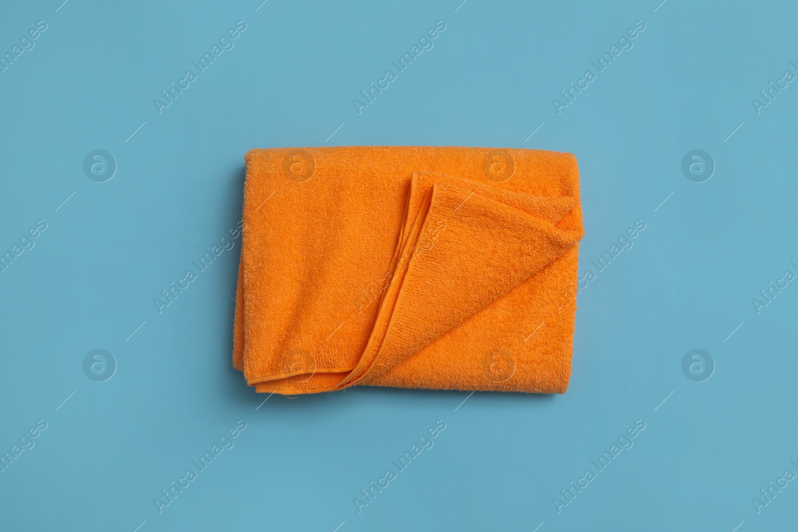 Folded orange beach towel on light blue background, top view Photo of Folded orange beach towel on light blue background, top view
