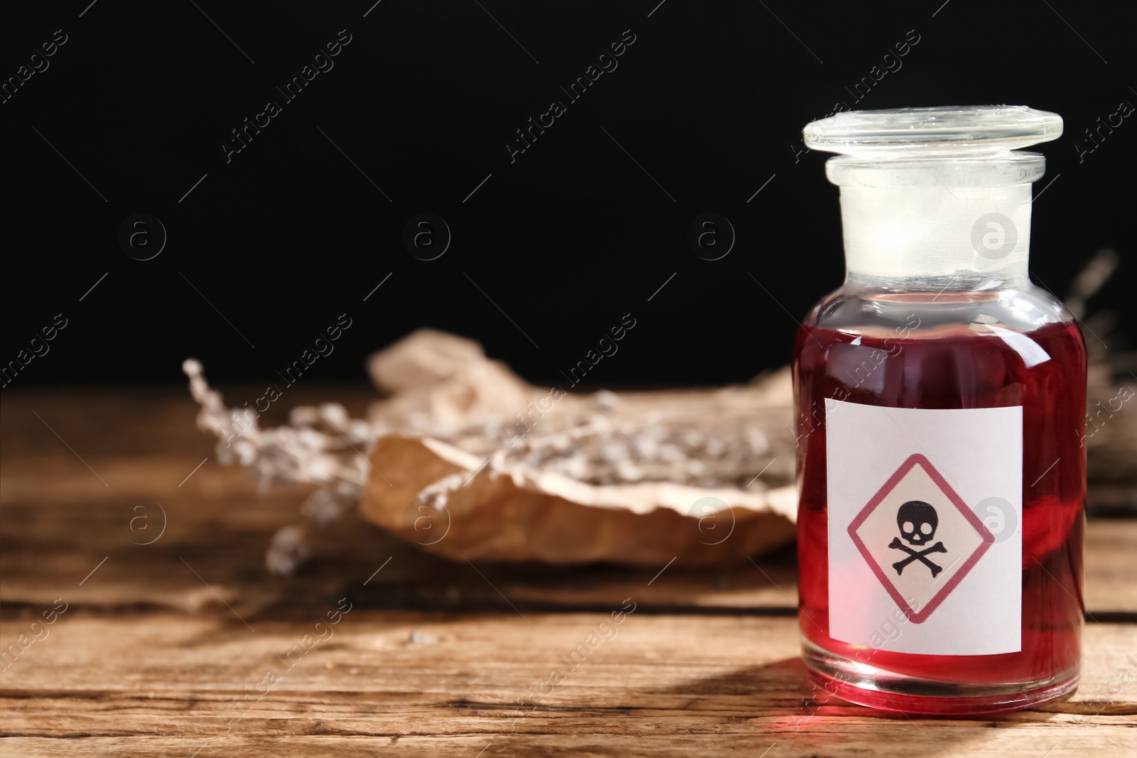 Glass bottle of poison with warning sign on wooden table. Space for text Photo of Glass bottle of poison with warning sign on wooden table. Space for text