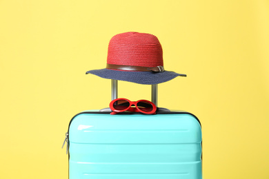 Photo of Turquoise suitcase with sunglasses and hat on yellow background