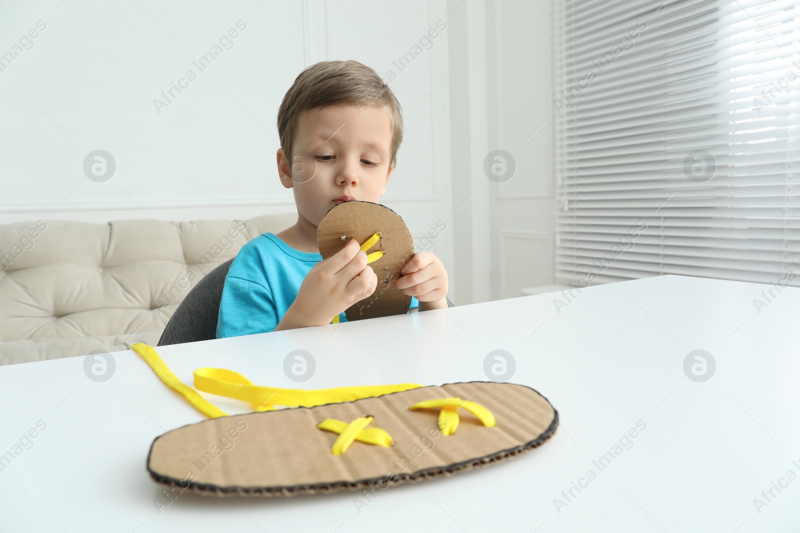 Little boy tying shoe lace using training cardboard template at white table indoors Photo of Little boy tying shoe lace using training cardboard template at white table indoors