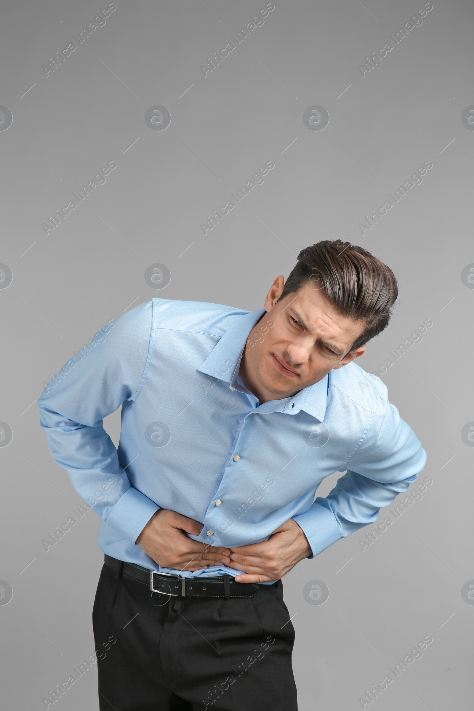 Young man suffering from abdominal pain on grey background Photo of Young man suffering from abdominal pain on grey background