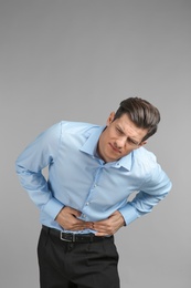 Young man suffering from abdominal pain on grey background Photo of Young man suffering from abdominal pain on grey background