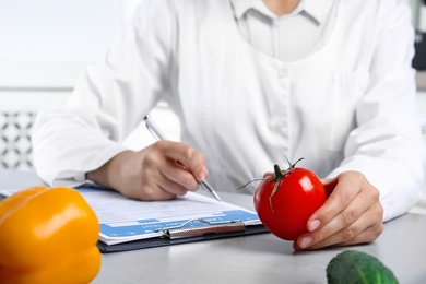 Scientist with laboratory test form and fresh tomato at table indoors, closeup. Poison detection Photo of Scientist with laboratory test form and fresh tomato at table indoors, closeup. Poison detection