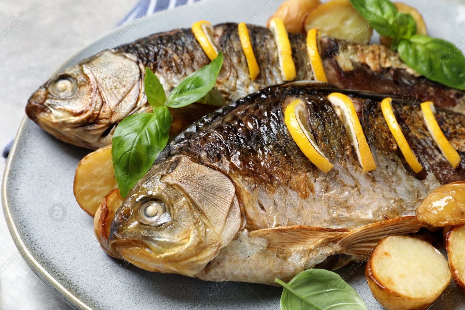 Tasty homemade roasted crucian carps with garnish on light grey table, closeup. River fish Photo of Tasty homemade roasted crucian carps with garnish on light grey table, closeup. River fish