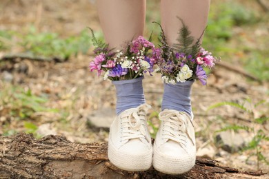 Woman standing on log with flowers in socks outdoors, closeup Photo of Woman standing on log with flowers in socks outdoors, closeup