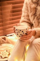 Photo of Woman with cup of hot drink and Christmas cookies at home, closeup