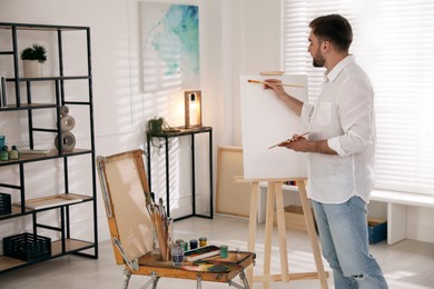 Young man painting on easel with brush in artist studio Photo of Young man painting on easel with brush in artist studio