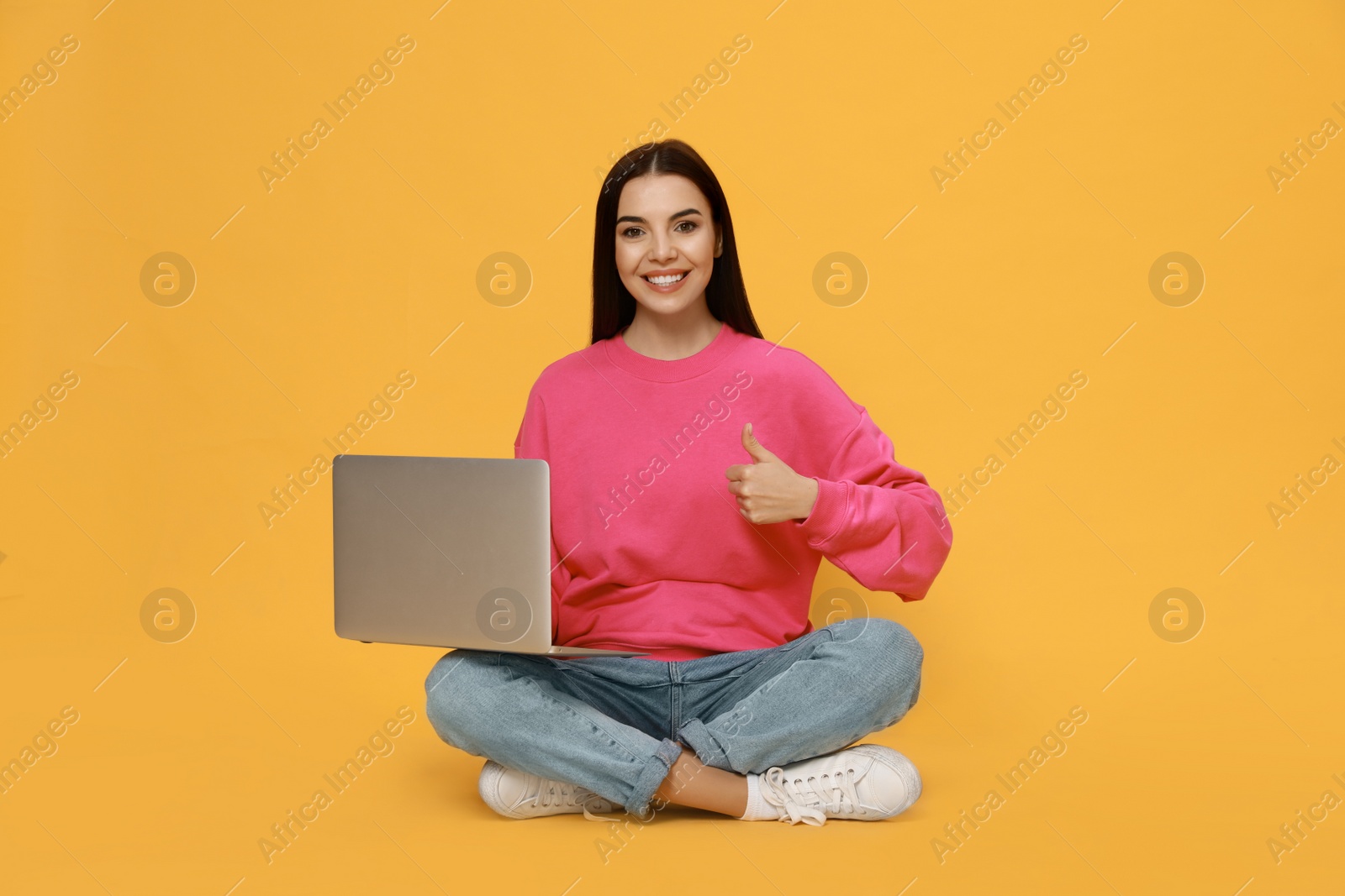 Young woman with modern laptop on yellow background Photo of Young woman with modern laptop on yellow background