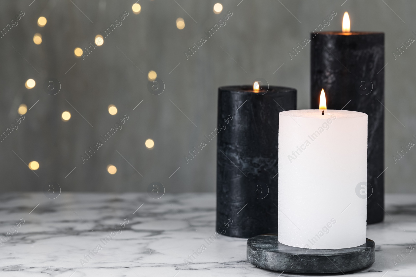 Burning candles on white marble table against blurred lights, space for text Photo of Burning candles on white marble table against blurred lights, space for text