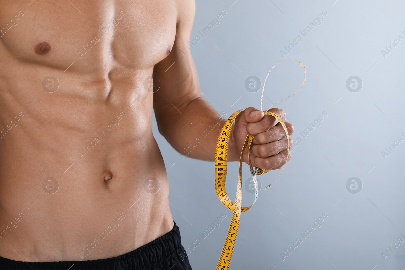 Shirtless man with slim body and measuring tape on grey background, closeup Photo of Shirtless man with slim body and measuring tape on grey background, closeup