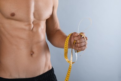 Shirtless man with slim body and measuring tape on grey background, closeup Photo of Shirtless man with slim body and measuring tape on grey background, closeup