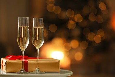 Glasses with champagne and Christmas gift on table in room, bokeh effect. Space for text Image of Glasses with champagne and Christmas gift on table in room, bokeh effect. Space for text