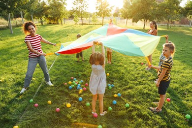 Group of children and teachers playing with rainbow playground parachute on green grass. Summer camp activity Photo of Group of children and teachers playing with rainbow playground parachute on green grass. Summer camp activity