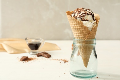 Delicious vanilla ice cream with toppings in wafer cone on white wooden table. Space for text Photo of Delicious vanilla ice cream with toppings in wafer cone on white wooden table. Space for text