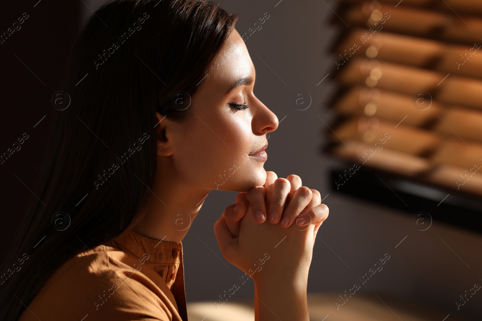 Photo of Religious young woman with clasped hands praying indoors