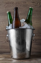 Metal bucket with bottles of beer and ice cubes on wooden table Photo of Metal bucket with bottles of beer and ice cubes on wooden table