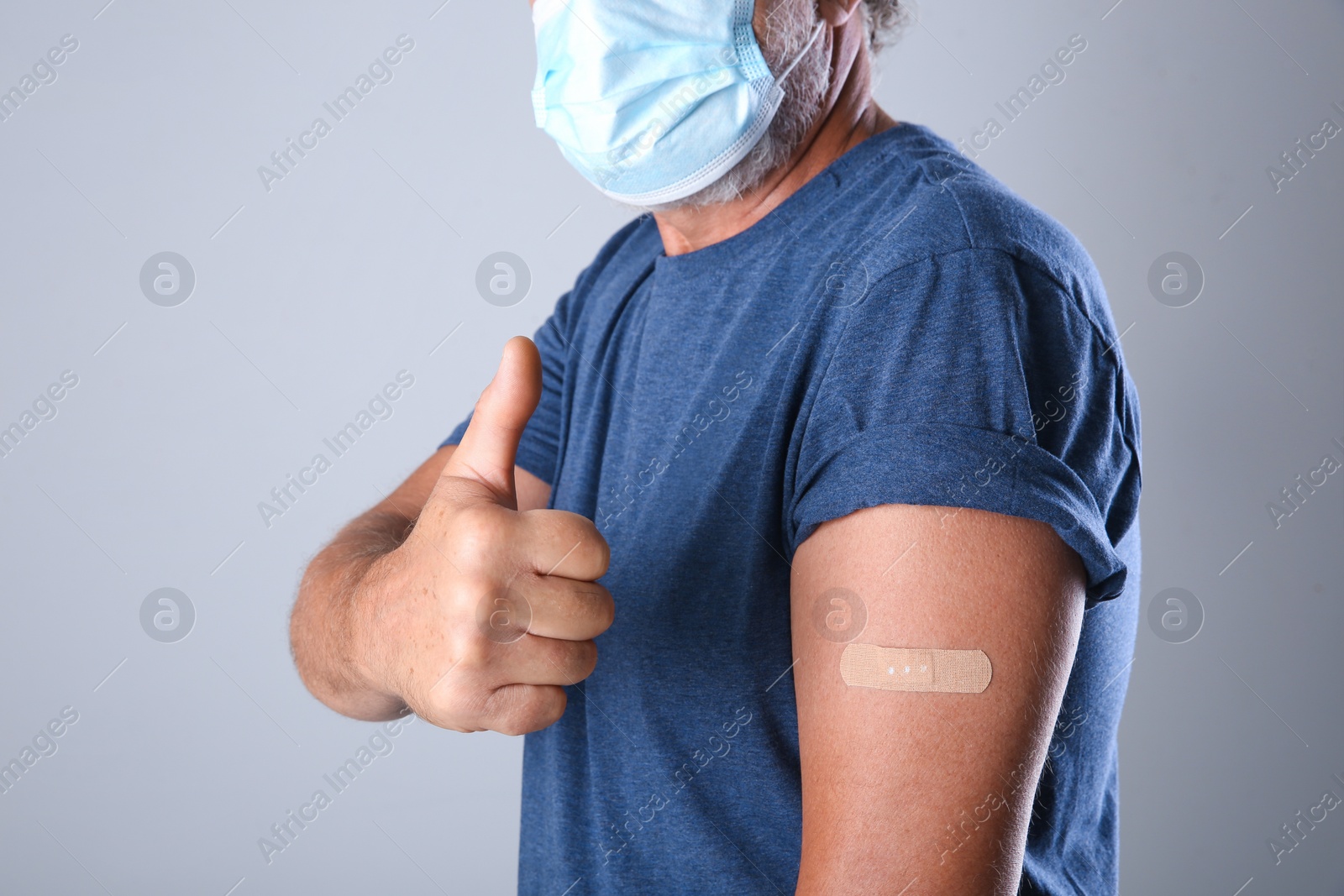 Senior man in protective mask showing arm with bandage after vaccination on grey background, closeup Photo of Senior man in protective mask showing arm with bandage after vaccination on grey background, closeup
