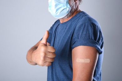 Senior man in protective mask showing arm with bandage after vaccination on grey background, closeup Photo of Senior man in protective mask showing arm with bandage after vaccination on grey background, closeup
