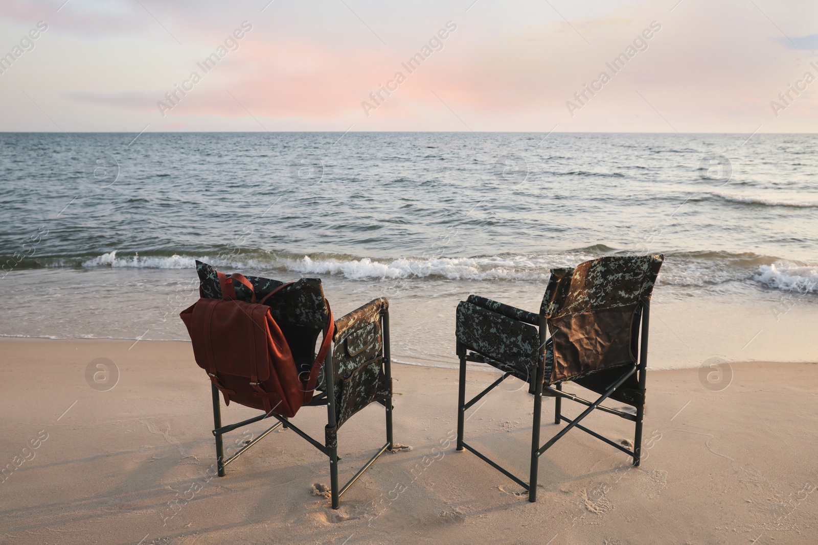 Camping chairs and backpack on sandy beach near sea Photo of Camping chairs and backpack on sandy beach near sea