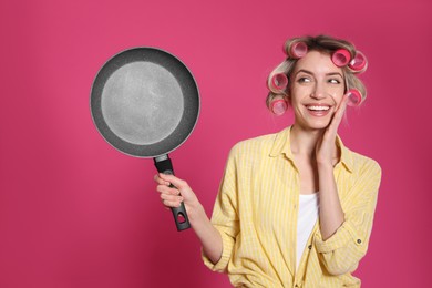 Young housewife with frying pan on pink background Photo of Young housewife with frying pan on pink background