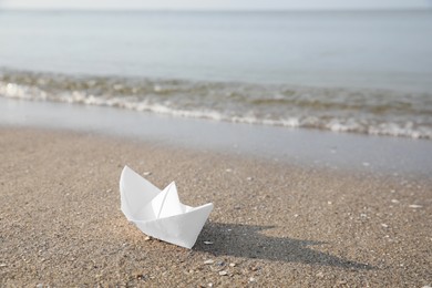 White paper boat on sandy beach near sea, space for text Photo of White paper boat on sandy beach near sea, space for text