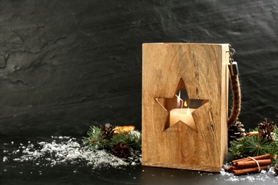 Photo of Wooden Christmas lantern with burning candle and festive decor on black background. Space for text