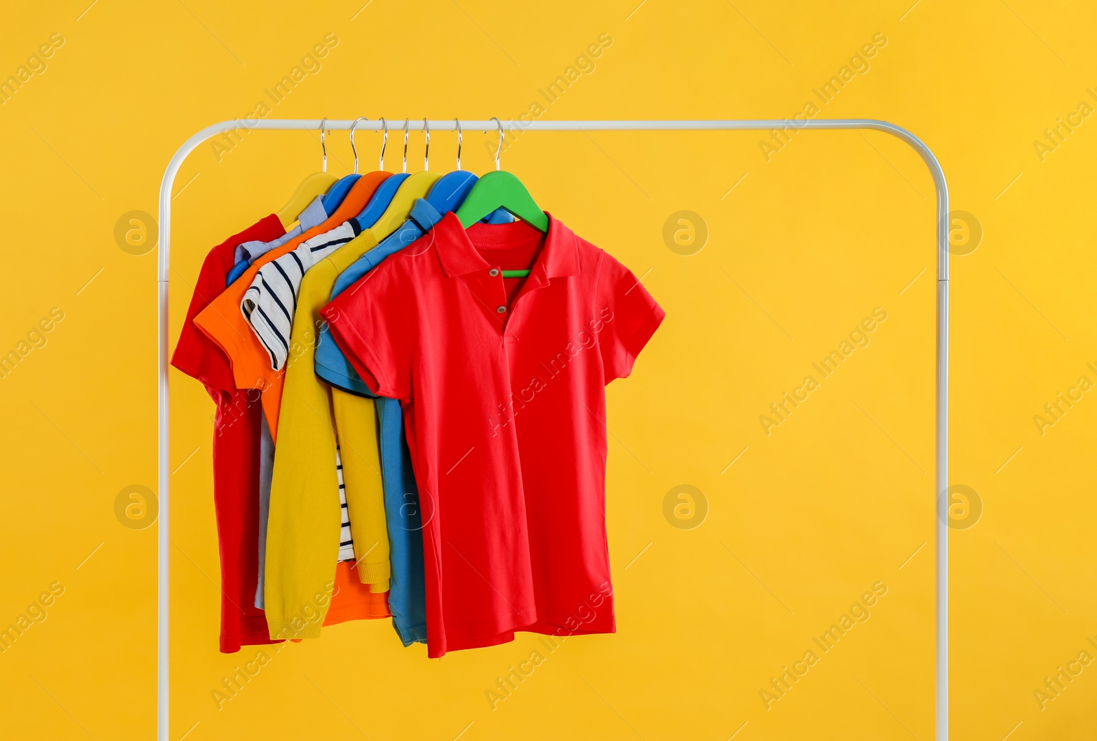 Photo of Rack with stylish children clothes on yellow background