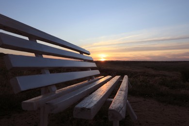 Wooden bench in field at sunrise, closeup. Early morning landscape Photo of Wooden bench in field at sunrise, closeup. Early morning landscape