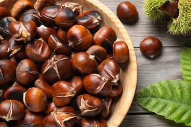 Delicious roasted edible chestnuts on brown wooden table, flat lay Photo of Delicious roasted edible chestnuts on brown wooden table, flat lay