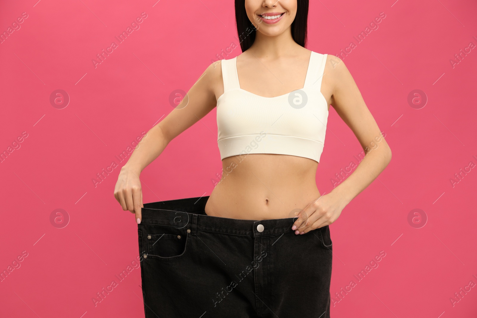 Happy young woman wearing big jeans after weight loss on pink background, closeup Photo of Happy young woman wearing big jeans after weight loss on pink background, closeup