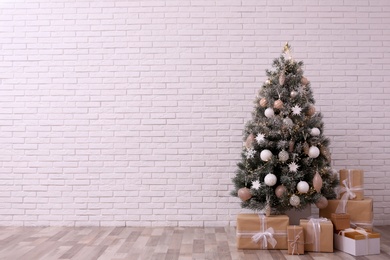 Beautifully decorated Christmas tree and gift boxes near white brick wall, space for text Photo of Beautifully decorated Christmas tree and gift boxes near white brick wall, space for text