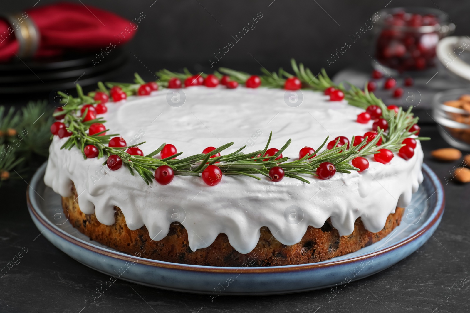 Photo of Traditional Christmas cake decorated with rosemary and cranberries on dark grey table, closeup